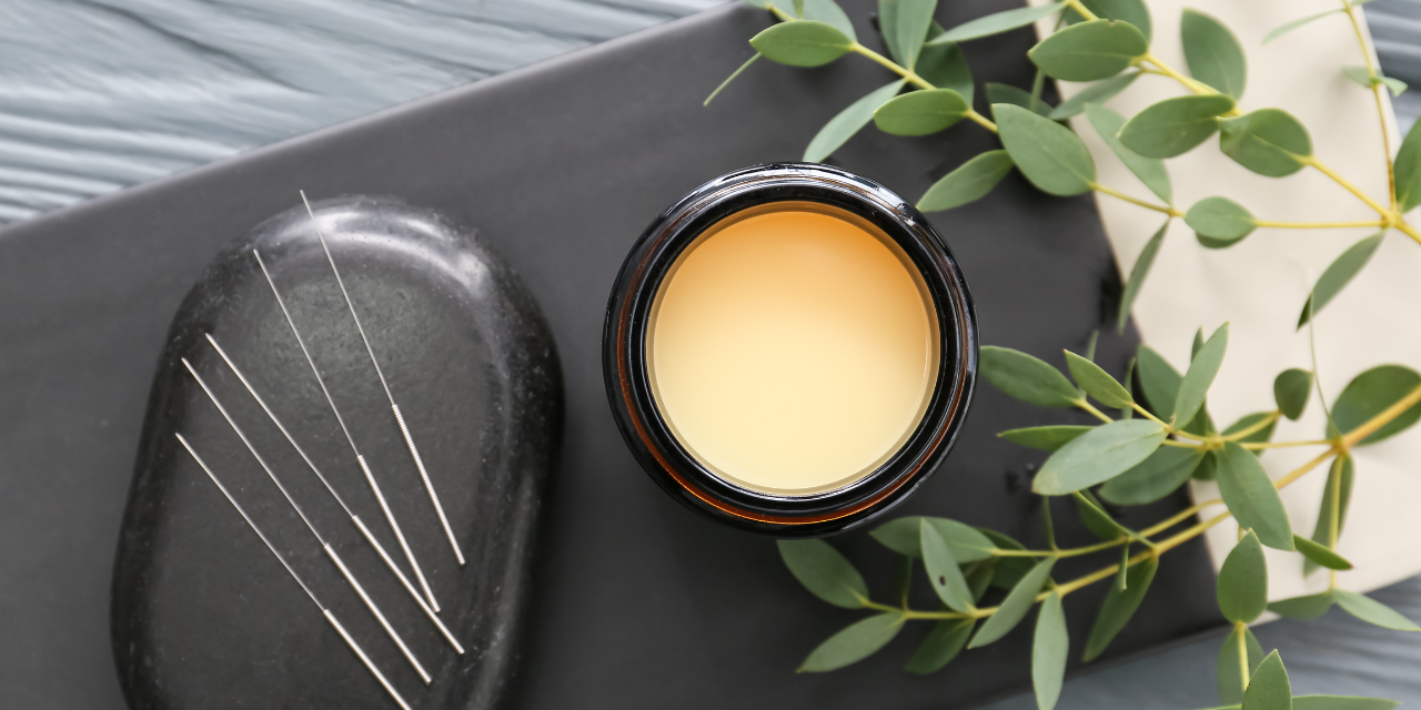 Acupuncture needles and a candle sitting on a table with greenery