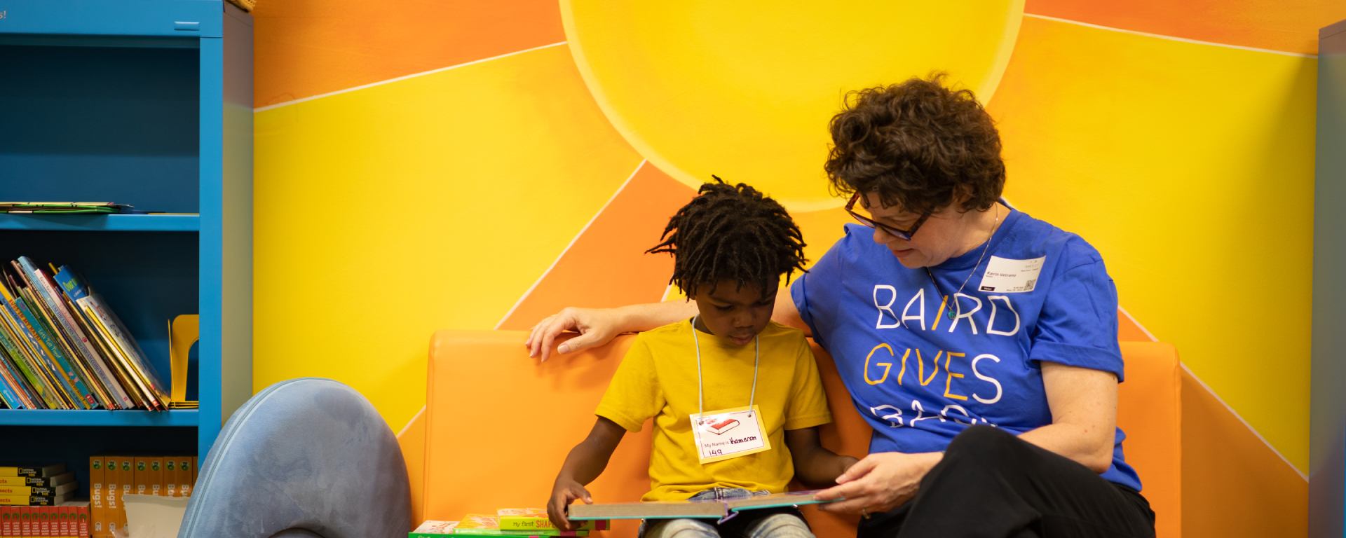 Woman in a Silver LakeCares t-shirt reading to a student.