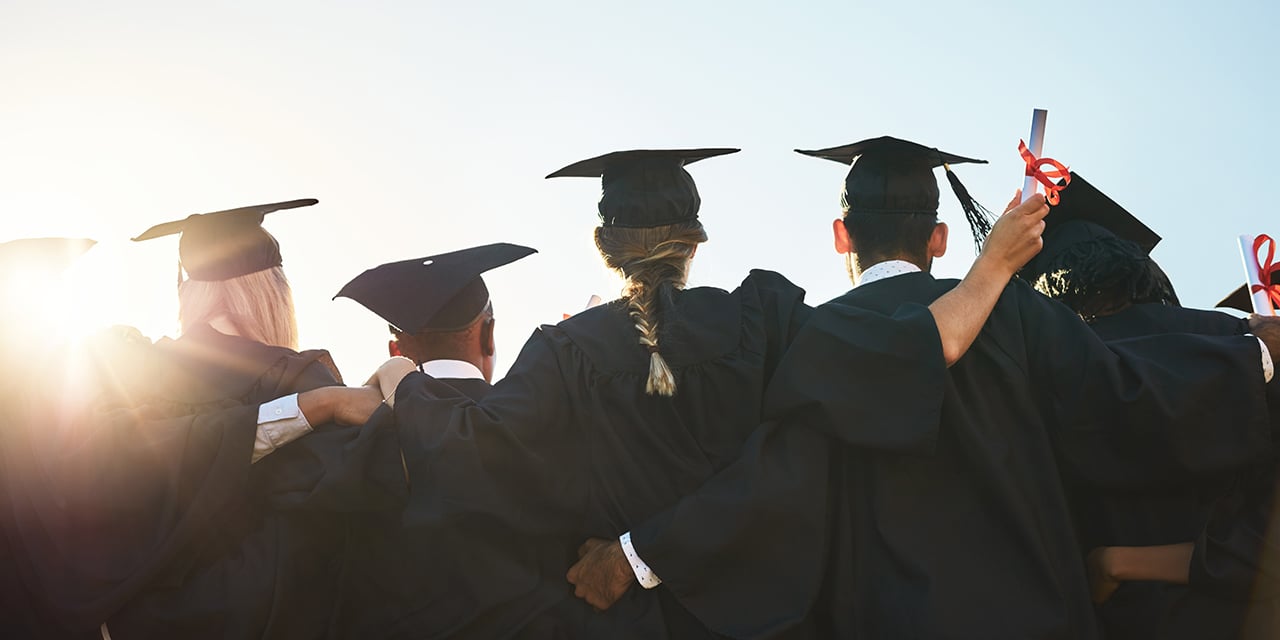 College graduates huddled together facing the sunset.